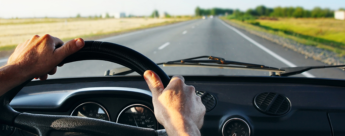 Manos de un hombre en el volante manejando en una carretera durante el día.